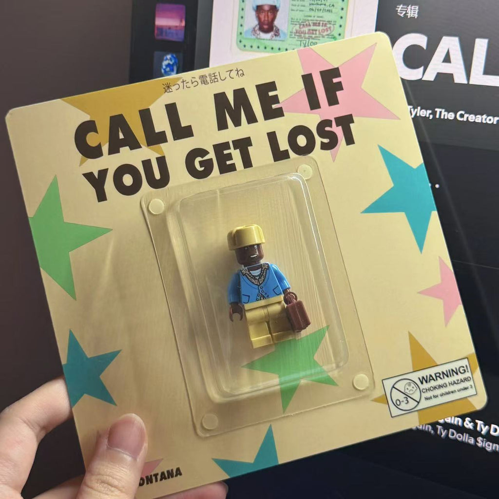 "Call Me If You Get Lost" custom minifigure in blue outfit, gold hat, and brown bag, held in packaging.