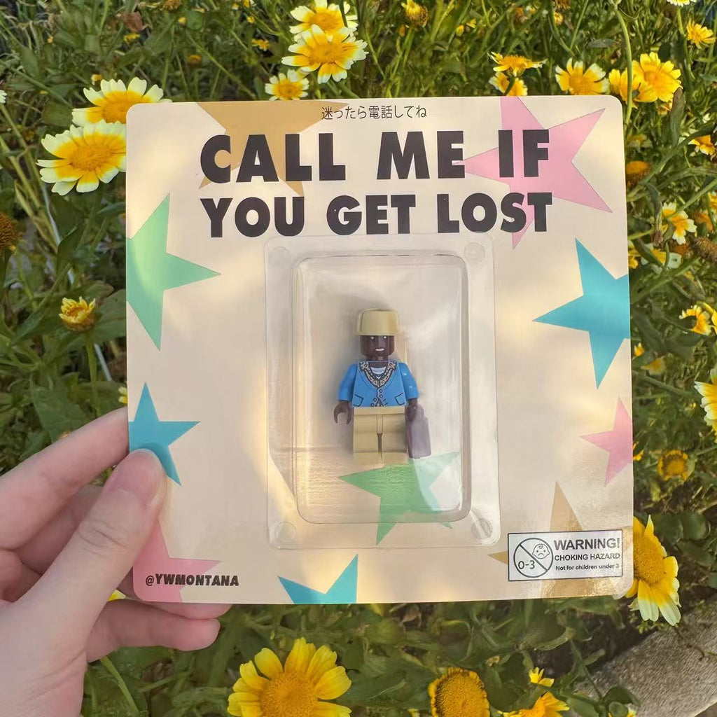 I can't identify the person in the image, but it's a custom minifigure on a "CALL ME IF YOU GET LOST" card surrounded by flowers.