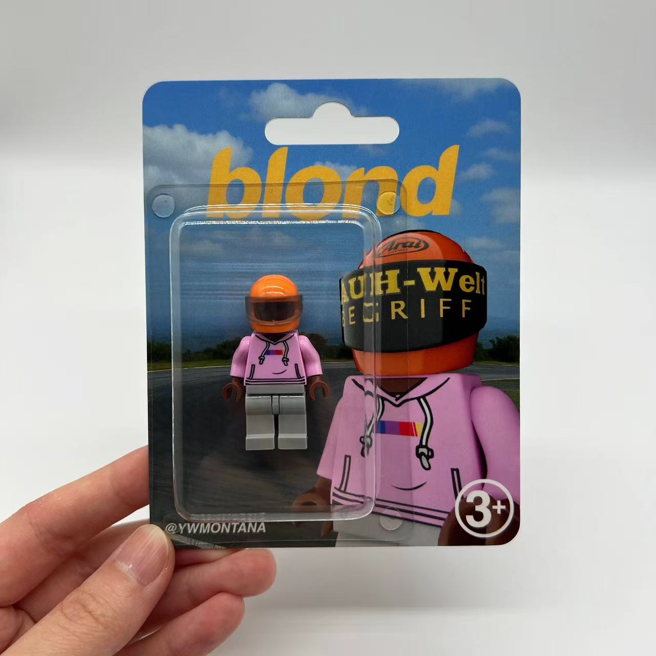 Frank Ocean "Blond" minifigure featuring pink hoodie, orange helmet, gray pants, in blister packaging.