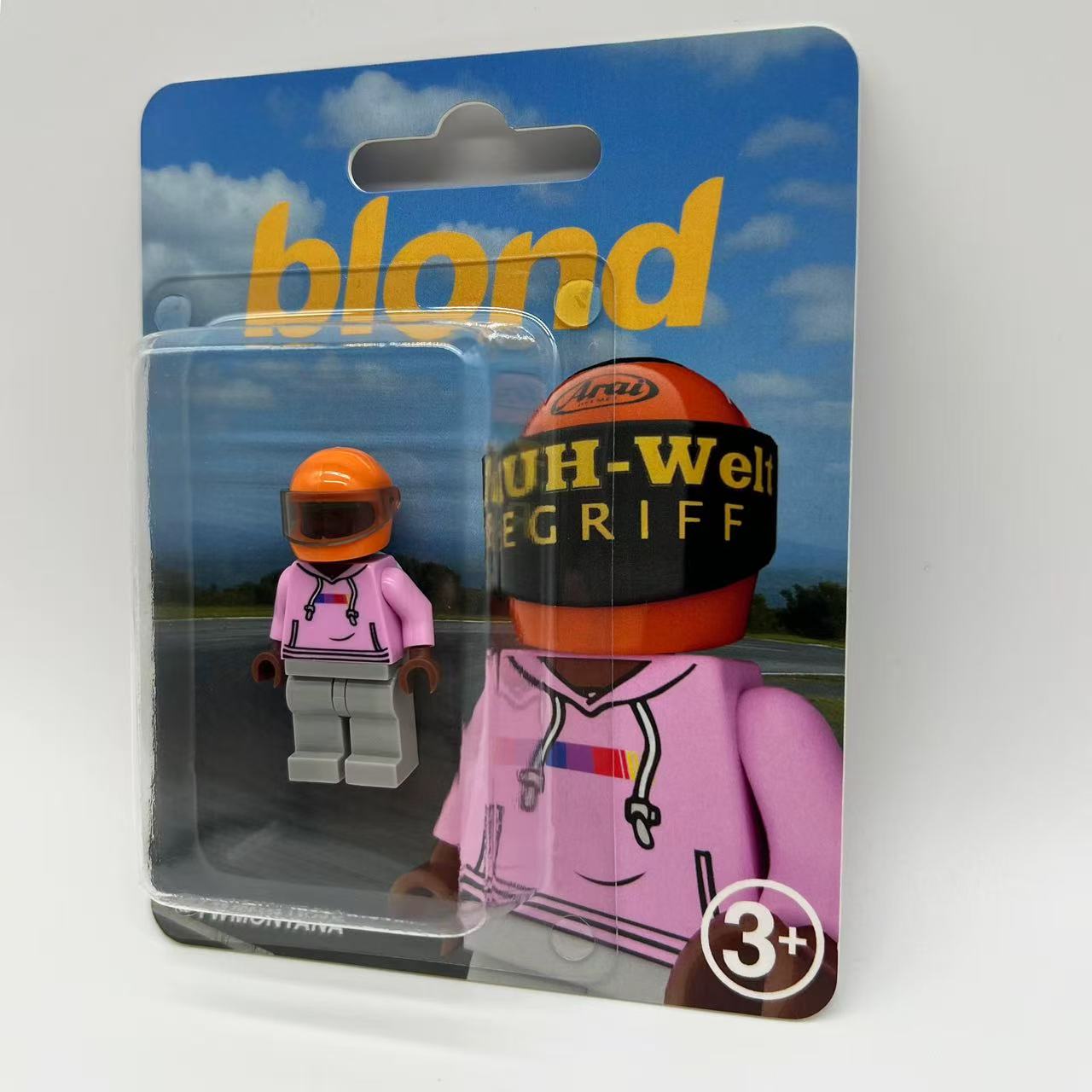 Frank Ocean "Blond" custom minifigure in pink hoodie, orange helmet, grey pants, blister packaging.